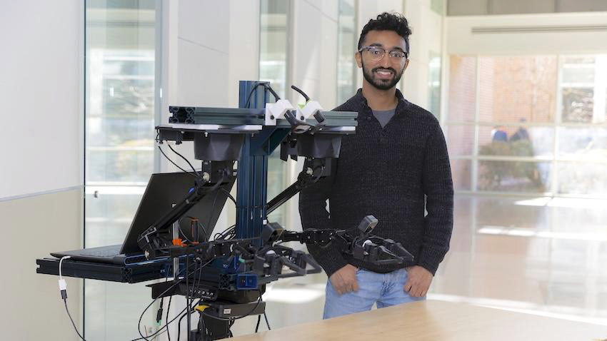 man standing infront of a computer and robit arm on a table